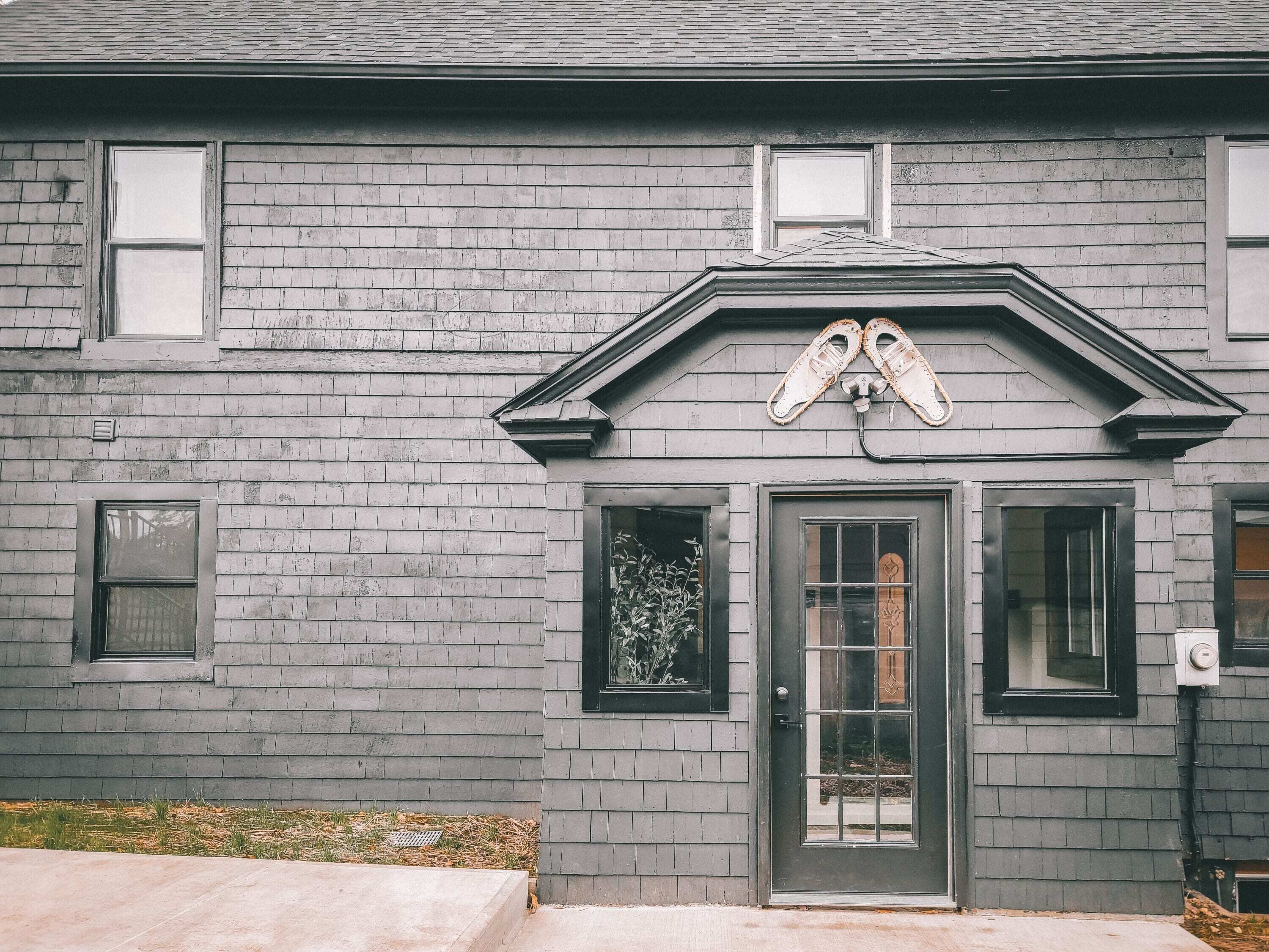 Una casa gris con puerta gris oscuro, dos ventanas y un pequeño porche.