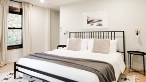 Ein Schlafzimmer mit Bett, Fenster mit Vorhängen, Nachttisch und Wandlampe.
