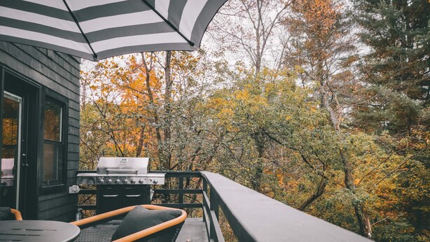 Eine Terrasse mit Grill, Sitzgelegenheit und Blick auf Herbstbäume.