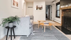 Ein modernes Wohnzimmer mit einem grauen Sofa, einem runden Holztisch und einem schwarz-weiß gestreiften Teppich.