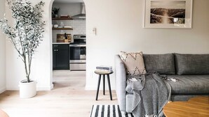 Ein modernes Wohnzimmer mit einem grauen Sofa, einem Couchtisch, einem Streifen Teppich und einem Topfpflanzen.