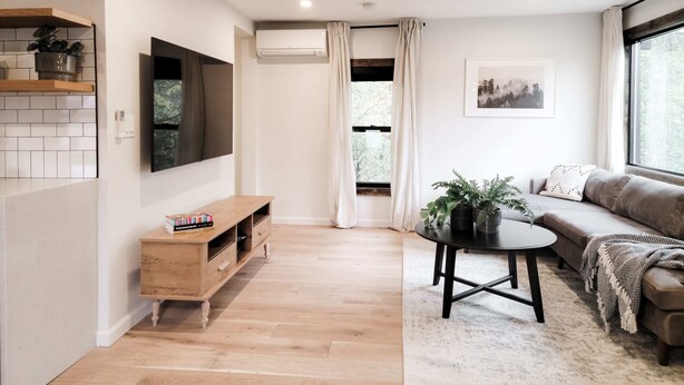 Una sala de estar moderna con piso de madera, un sofá, una mesita de centro y un televisor montado en la pared.