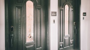 Dos puertas de madera oscura con parte superior arqueada y un panel de vidrio central. Cada puerta tiene una pequeña placa encima que indica el número del apartamento.