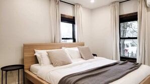 Un dormitorio moderno con estructura de cama de madera, ropa de cama blanca y una manta de punto marrón.