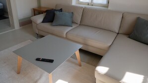 En stue med en beige sofa, et lille træsidebord og et gråt sofabord.