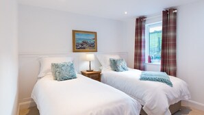 A bedroom with two beds, a painting on the wall, a window with curtains, and a nightstand with a lamp.