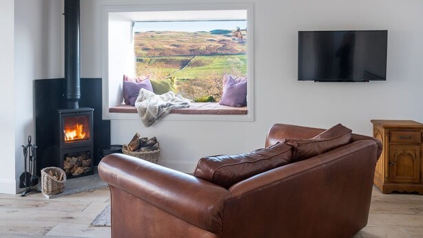 A living room with a fireplace, a sofa, a television, and a window with a view of the countryside.