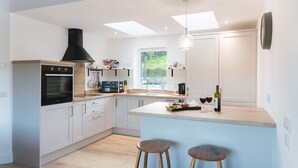 A modern kitchen with white cabinets, a black range hood, a microwave, and a coffee maker. There is a window providing natural light and a view of greenery outside.