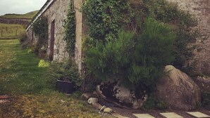 A stone building with a sloped roof, surrounded by greenery and a rural landscape.