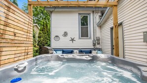 Un jacuzzi en un patio trasero con terraza de madera y una casa al fondo.