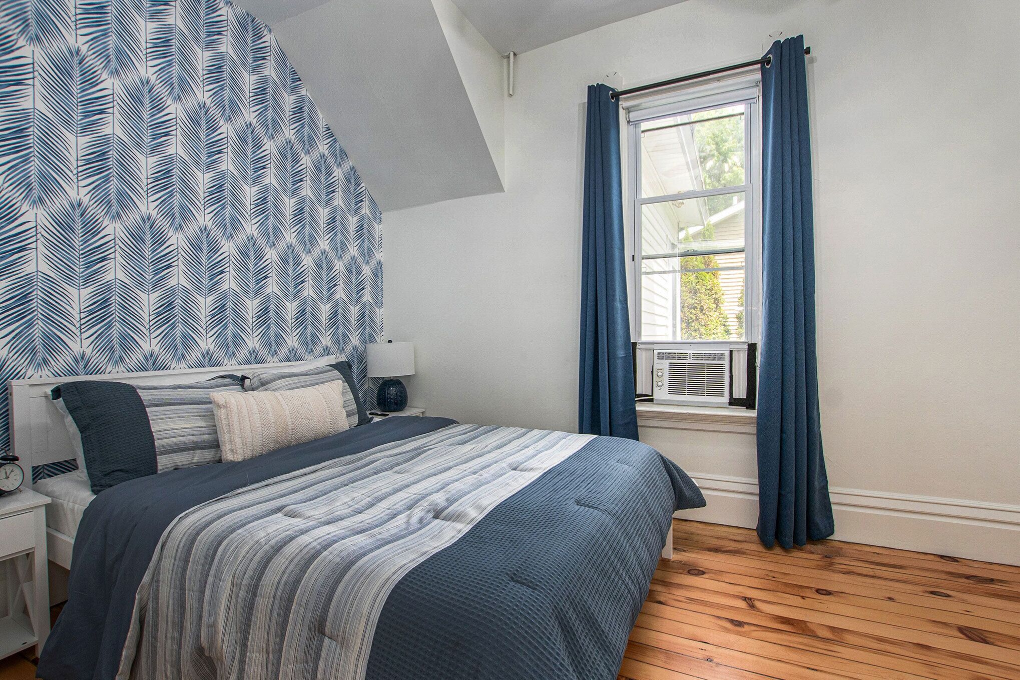 Quarto com cama, mesa de cabeceira e janela com cortinas.
