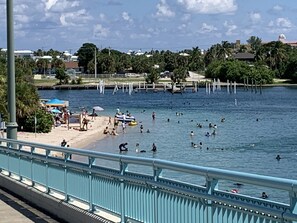 A waterfront area with a beach, people swimming, and a bridge with railings.