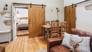 A cozy room with a wooden floor, a brown leather sofa, a wooden dining table with chairs, and a bed with white bedding. - Yr Hen Oriel (Caernarfon)
