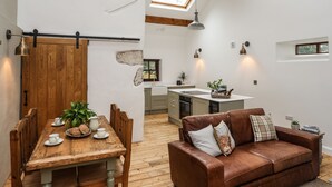 A modern kitchen with a central island, wooden dining table with chairs, and a brown leather sofa. - Yr Hen Oriel (Caernarfon)