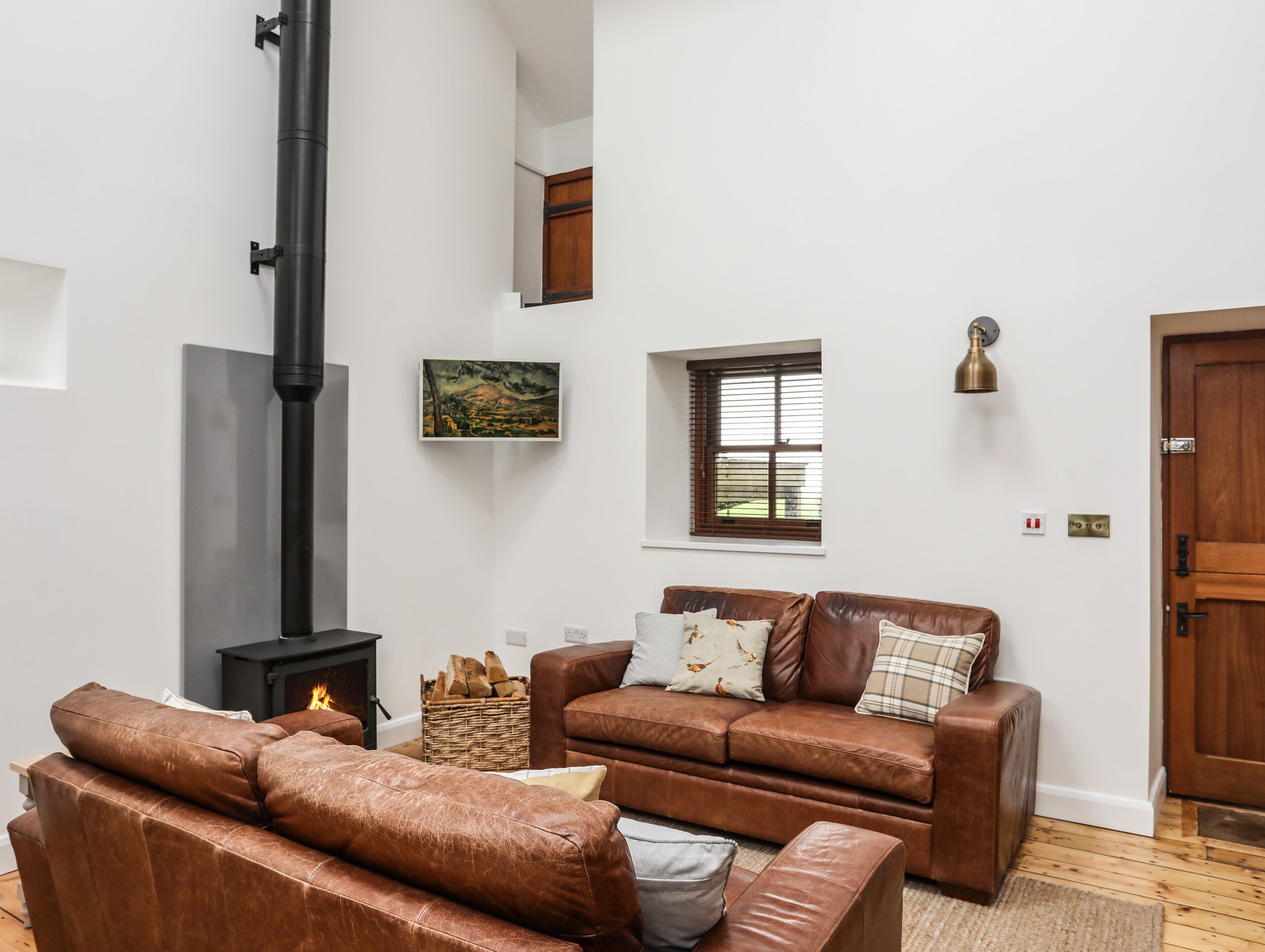 A living room with a fireplace, brown leather sofas, a painting, and a wooden door.