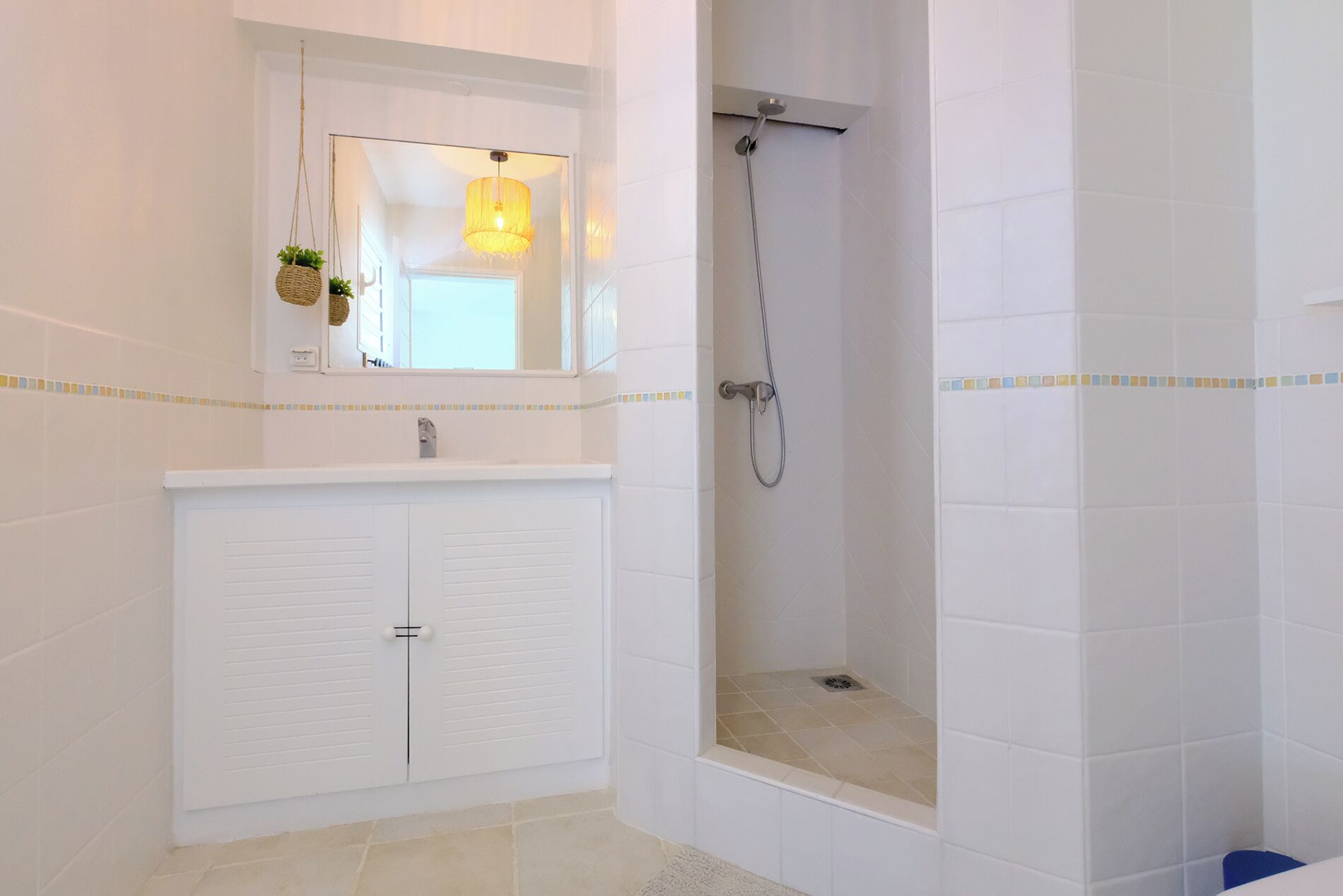 Un baño con tocador blanco, ducha y lámpara colgante.