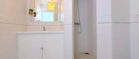 Un baño con tocador blanco, ducha y lámpara colgante.