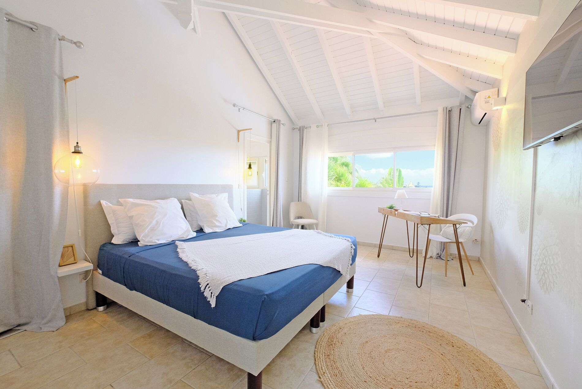 A bedroom with a bed, bedside tables, a desk, and a view of the outdoors.