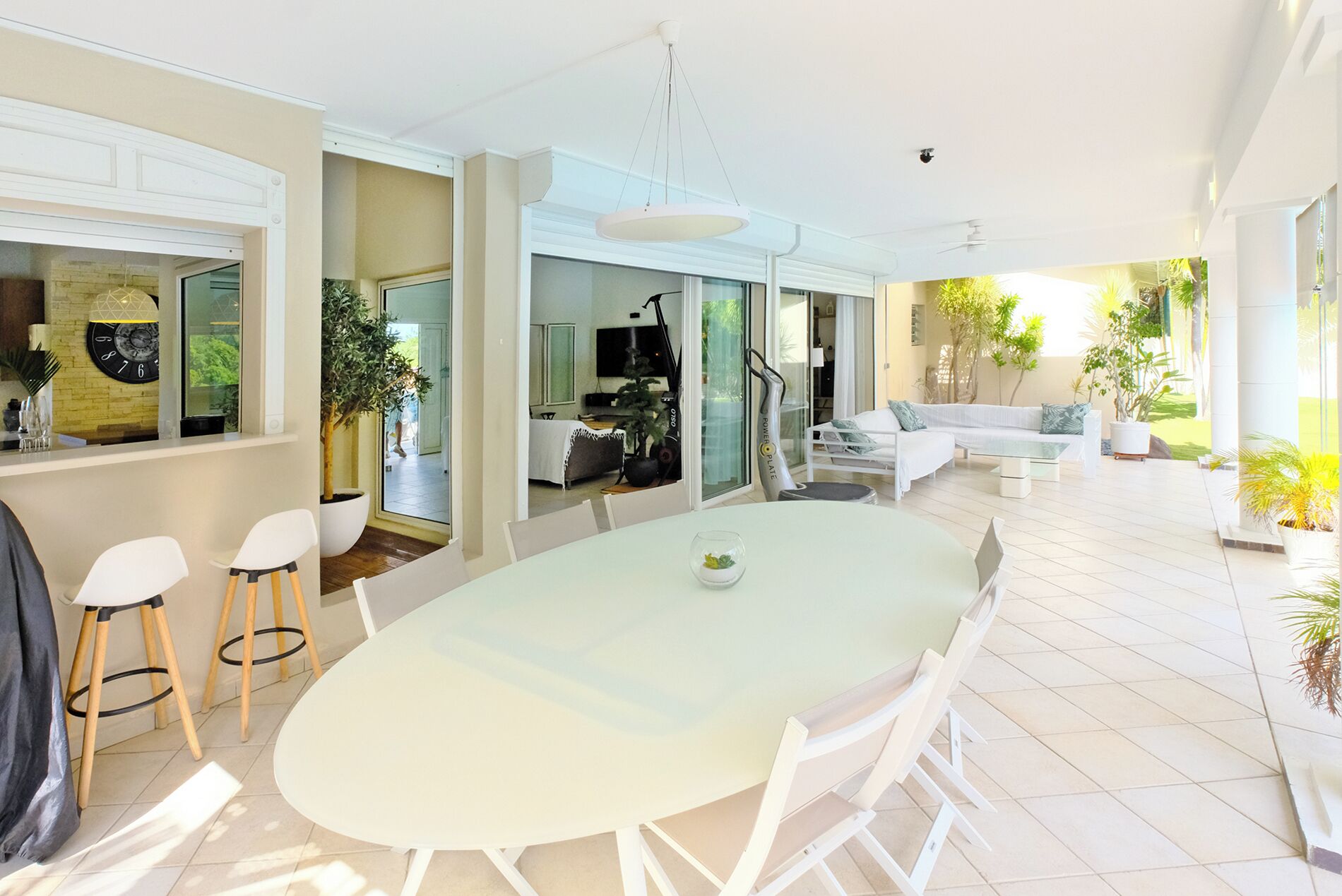 A spacious living area with a large round table, white furniture, and a view of the outdoors.