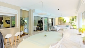 A spacious living area with a large round table, white furniture, and a view of the outdoors.