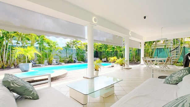 A modern outdoor lounge area with a pool, white furniture, and tropical plants.