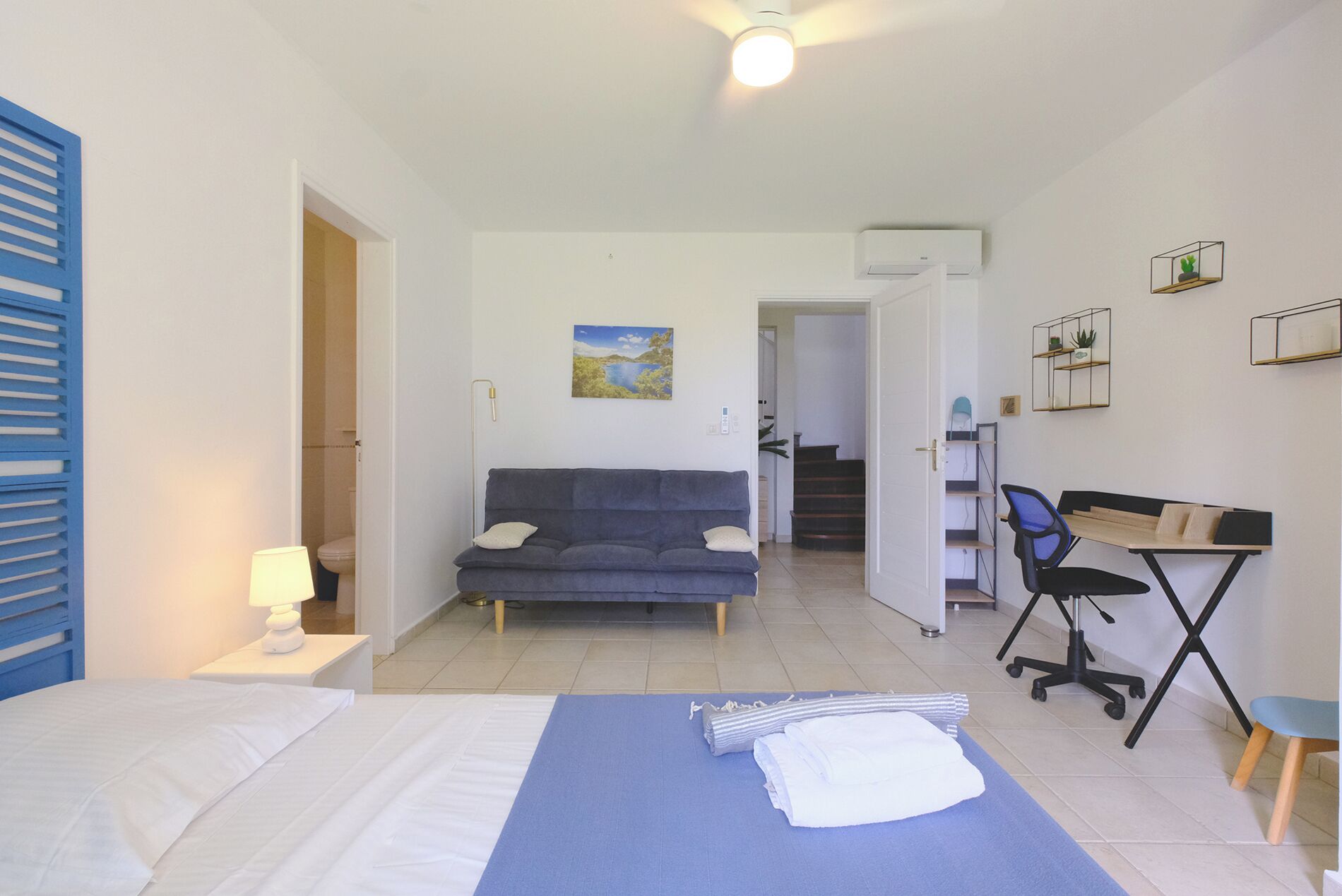 A room with a bed, a desk, a sofa, and a staircase leading to another area.