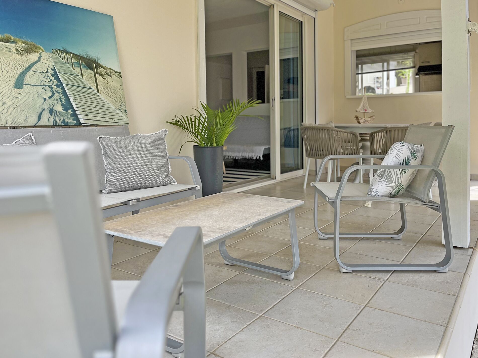 A sunlit patio with modern furniture, a potted plant, and a painting of a beach scene.