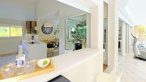 A modern kitchen with a large window, a dining area with chairs, and a counter with a bottle and glasses.