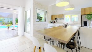 A modern kitchen with a large wooden table, white cabinets, and pendant lighting.