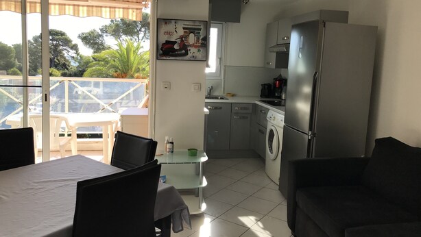 Een compacte woonruimte met een eethoek, een keuken met moderne apparatuur en een balkon met uitzicht op bomen en een gebouw.