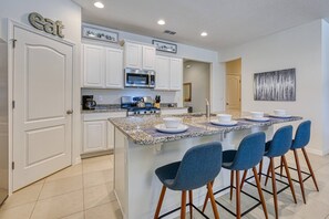 Una cocina moderna con armarios blancos, encimera de granito y una isla central con taburetes de bar.