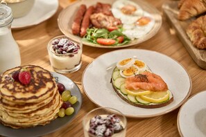 A breakfast table with pancakes, smoked salmon, eggs, and a variety of fruits and vegetables. - GrandeMar Suites (Astypalaia)