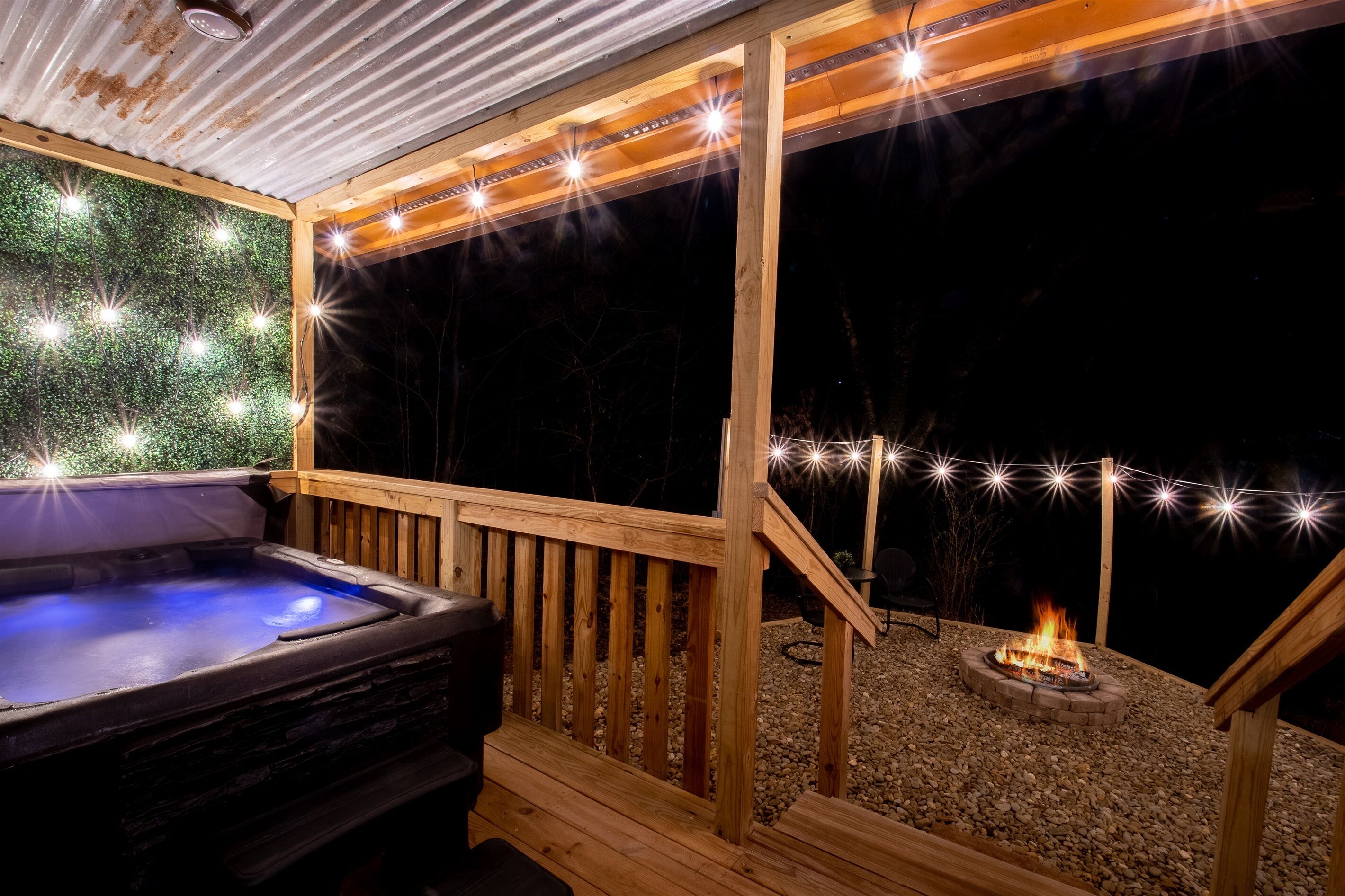 Une terrasse en bois avec un jacuzzi, des guirlandes lumineuses et un foyer extérieur.
