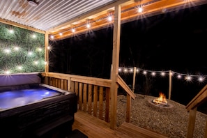 Een houten terras met een jacuzzi, lichtjes en een vuurkuil.