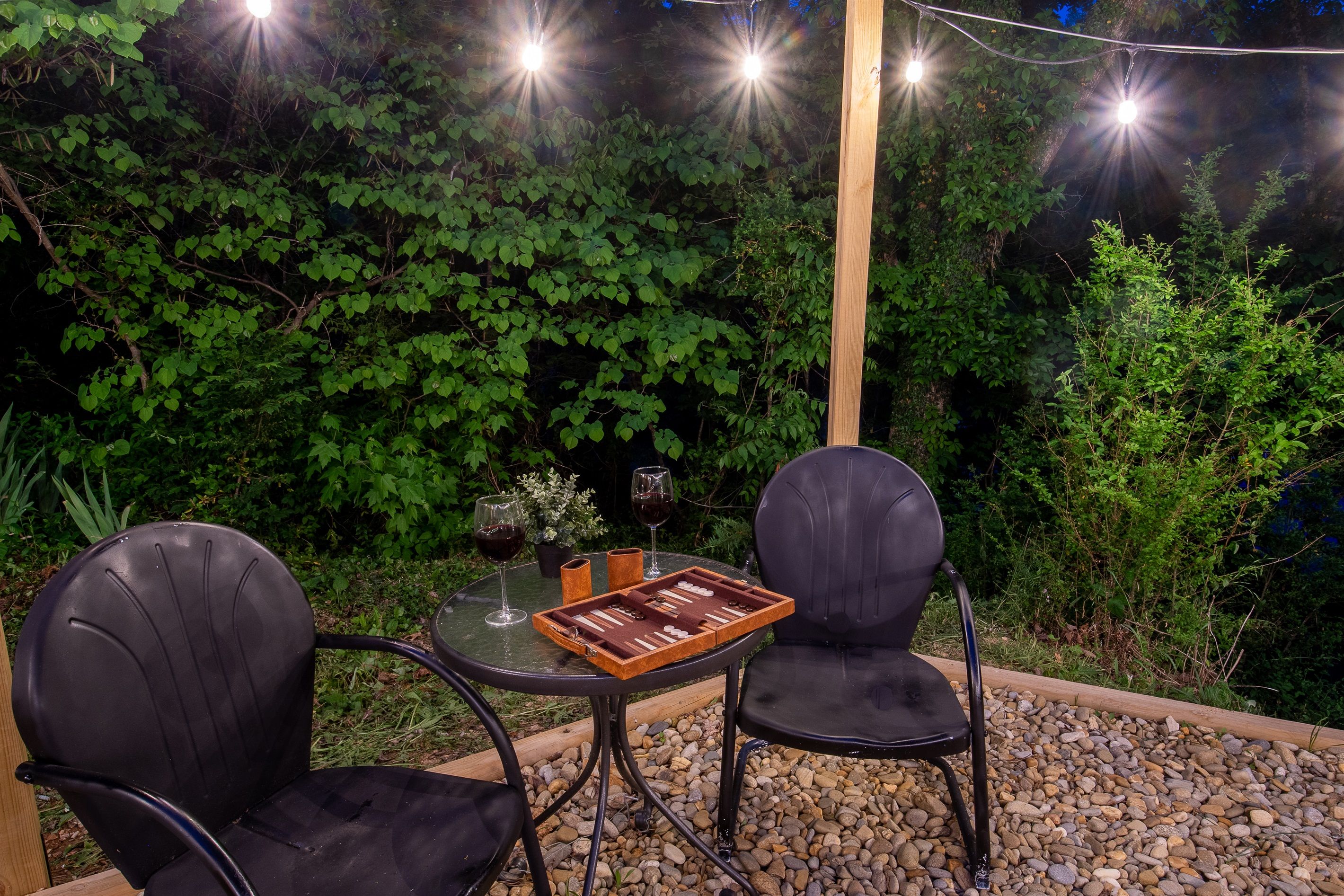 Un espace extérieur aménagé avec deux chaises et une table, entouré de verdure et illuminé par une guirlande lumineuse.