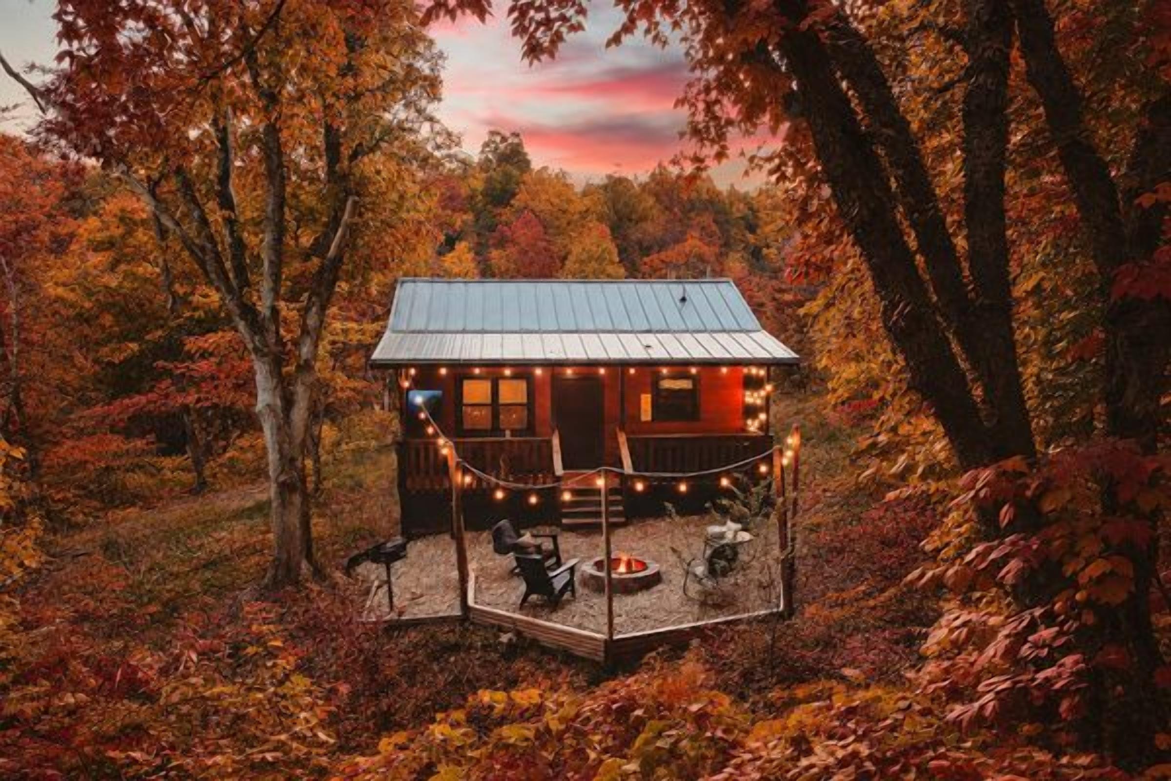 A cabin with a deck, surrounded by trees and a sunset.