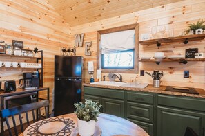 Una cocina acogedora de estilo cabaña con paredes de madera, un refrigerador negro, una cafetera y una ventana con vistas.