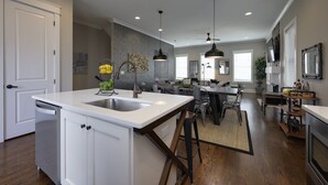 A modern kitchen with white cabinetry, a central island, and a dining area with a high ceiling and pendant lighting. - Walk2Germantown Rooftop Firepit Downtown Skyline King Suite 2-Car Garage (Nashville)