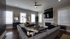A modern living room with a sectional sofa, a coffee table, and a fireplace. - Walk2Germantown Rooftop Firepit Downtown Skyline King Suite 2-Car Garage (Nashville)