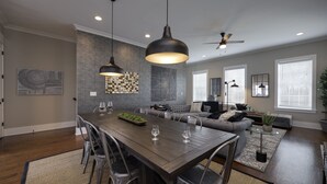 A modern living room with a dining area, grey sofas, a wooden dining table, and pendant lighting. - Walk2Germantown Rooftop Firepit Downtown Skyline King Suite 2-Car Garage (Nashville)