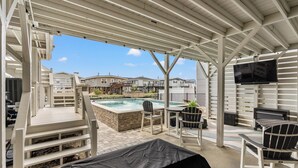 A covered outdoor area with a pool, seating, and a TV screen.