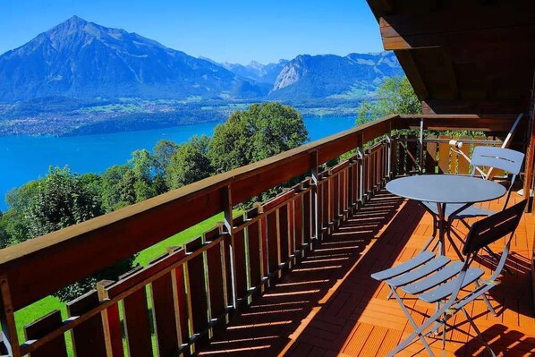 A wooden deck with a table and chairs overlooking a lake and mountains. - 2-Storey Chalet Apartment Near Interlaken · Panoramic Lake Thun & Jungfrau Views (Tschingel ob Gunten)