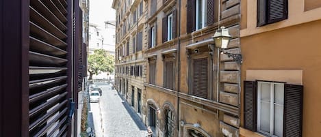 A narrow street with buildings on either side, featuring arched windows and shutters.