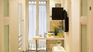 A kitchen with a white countertop, a black TV mounted on the wall, and a window with sheer curtains.