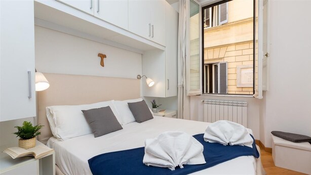 A neatly arranged bedroom with a bed, bedside tables, a window with shutters, and a radiator.