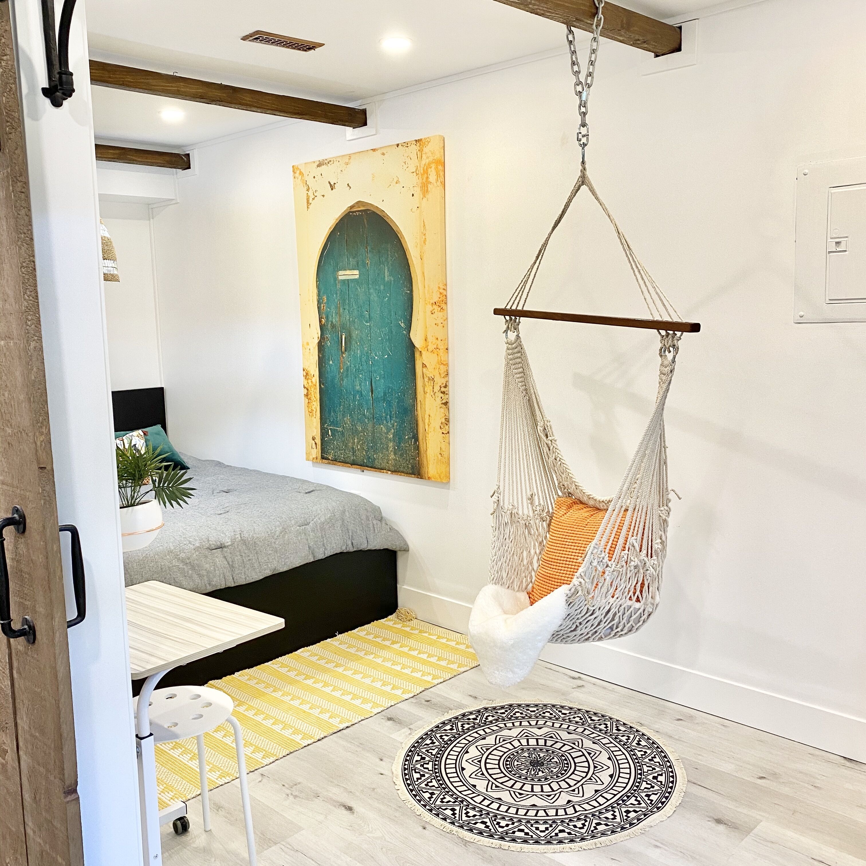 A cozy room with a hanging chair, a bed, a small table, and a decorative rug.