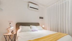 Ett hotellrum med en säng, en sänglampa, en luftkonditioneringsanläggning och ett fönster med gardiner.