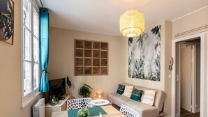 Ein Wohnzimmer mit einer Couch, einem Fernseher, einem Tisch mit einer Vase und einem großen Gemälde an der Wand.