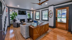 A modern living room with a wooden reception desk, grey sofas, a fireplace, and large windows.