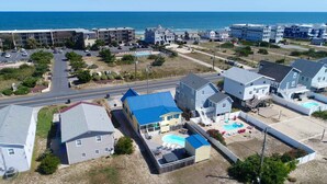 A residential area with houses, a swimming pool, and a beach in the background.